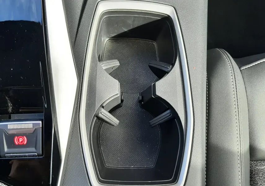 Gros plan sur les porte-gobelets centraux du Peugeot 5008 Hybrid 2025 en gris titane, avec sellerie noire visible.