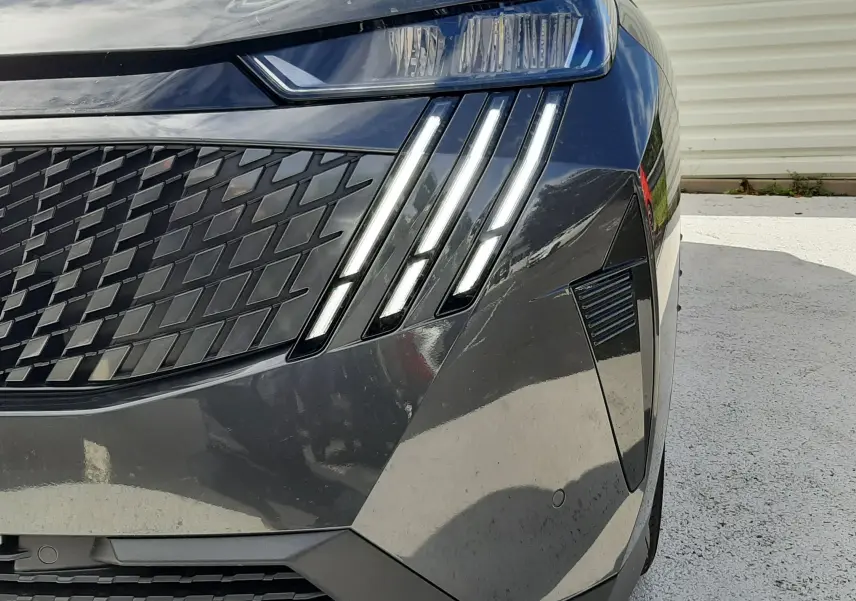 Gros plan sur l'avant droit gris titane métallisé du Peugeot 5008 Hybrid avec ses phares LED à griffes distinctives.