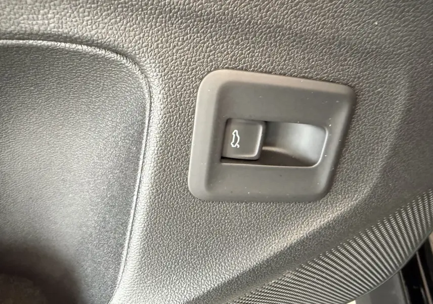 Gros plan sur le bouton d'ouverture du coffre intérieur en plastique noir texturé d'un Volkswagen T-Roc R-Line.