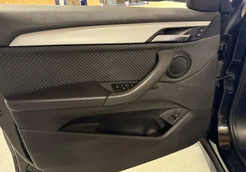 Vue rapprochée de la porte avant gauche noire d'une BMW X1 F48 2019 avec garniture tissu et commandes de vitres.