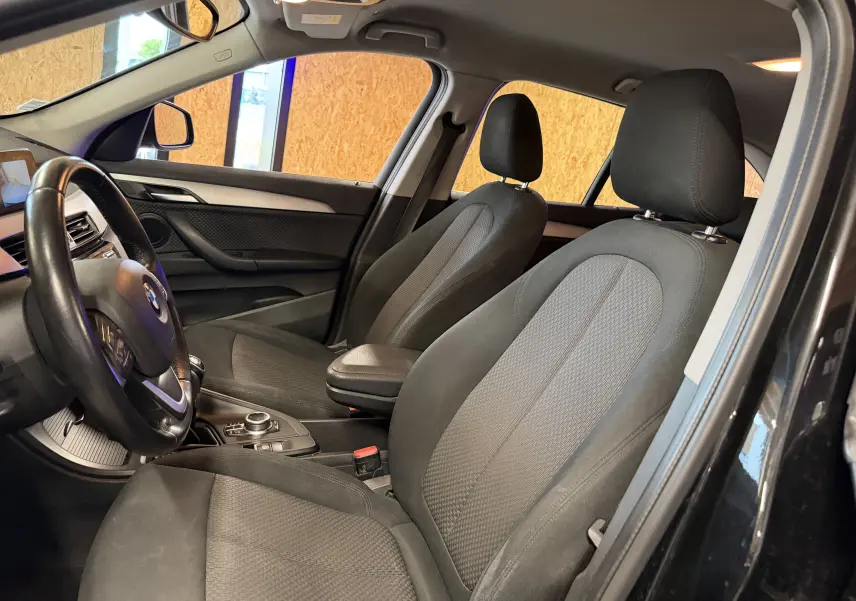 Vue intérieure côté conducteur du BMW X1 noir 2019, montrant les sièges avant en tissu et le tableau de bord.