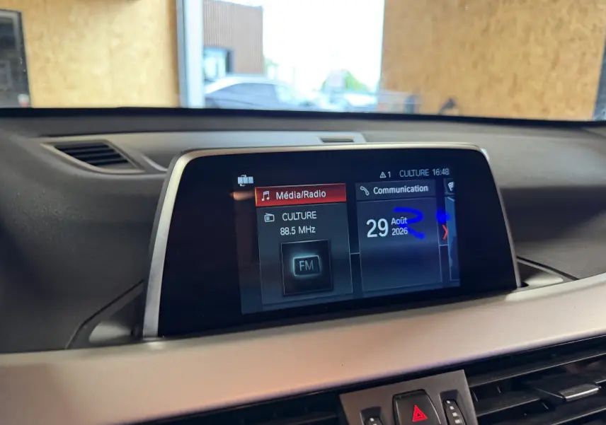Écran central du tableau de bord du BMW X1 noir (F48) 2019, affichant radio FM et date, vue intérieure frontale.