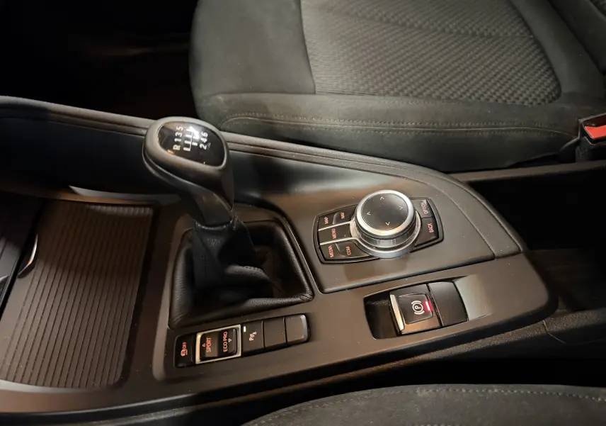 Vue rapprochée de la console centrale noire d’une BMW X1 2019 avec levier de vitesse manuel et commandes iDrive.