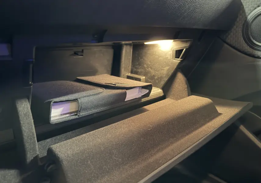 Gros plan sur la boîte à gants ouverte du BMW X1 noir 2019, avec un manuel dans une pochette textile et un éclairage intérieur.