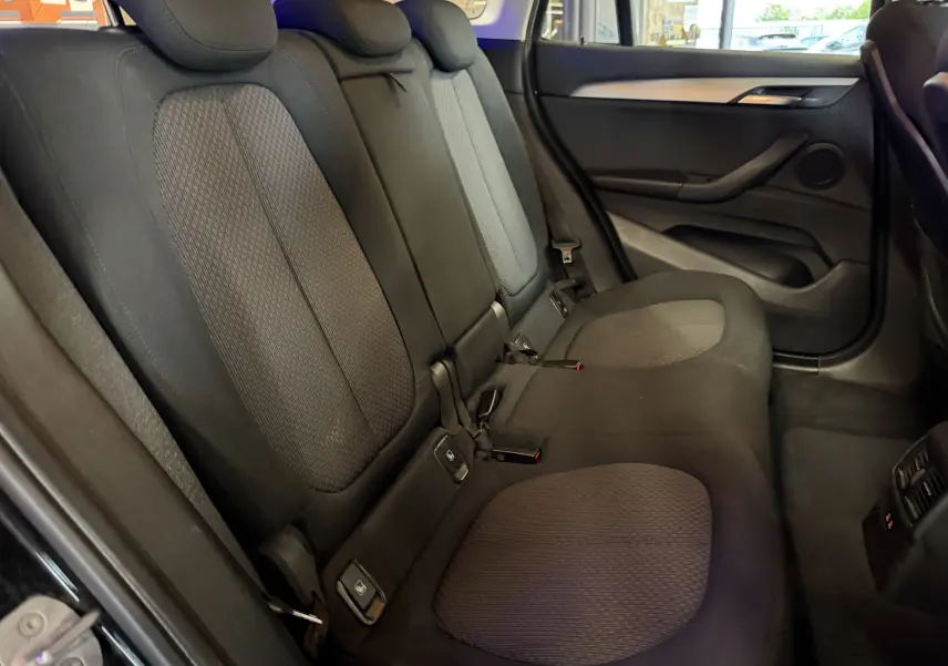 Vue intérieure côté droit des sièges arrière noirs en tissu du BMW X1 F48 2019, avec habillage de porte et ceintures visibles.