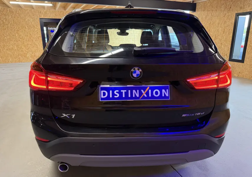 Vue arrière d'un BMW X1 noir 2019 avec feux allumés et logo SDrive16d visible sur le hayon.