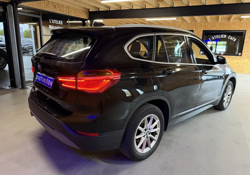 BMW X1 noir vue 3/4 arrière droit dans un garage, avec feux arrière allumés et jantes alliage.