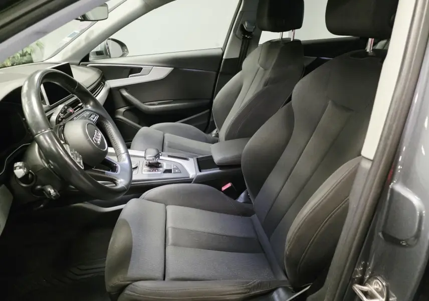 Vue intérieure côté gauche de l'Audi A4 Avant gris, montrant les sièges avant en tissu et le volant multifonction cuir.