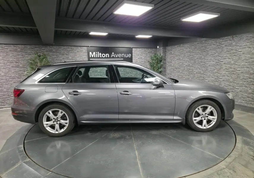Audi A4 Avant gris métallisé vue de profil côté gauche, jantes alu 17 pouces et intérieur visible en arrière-plan.