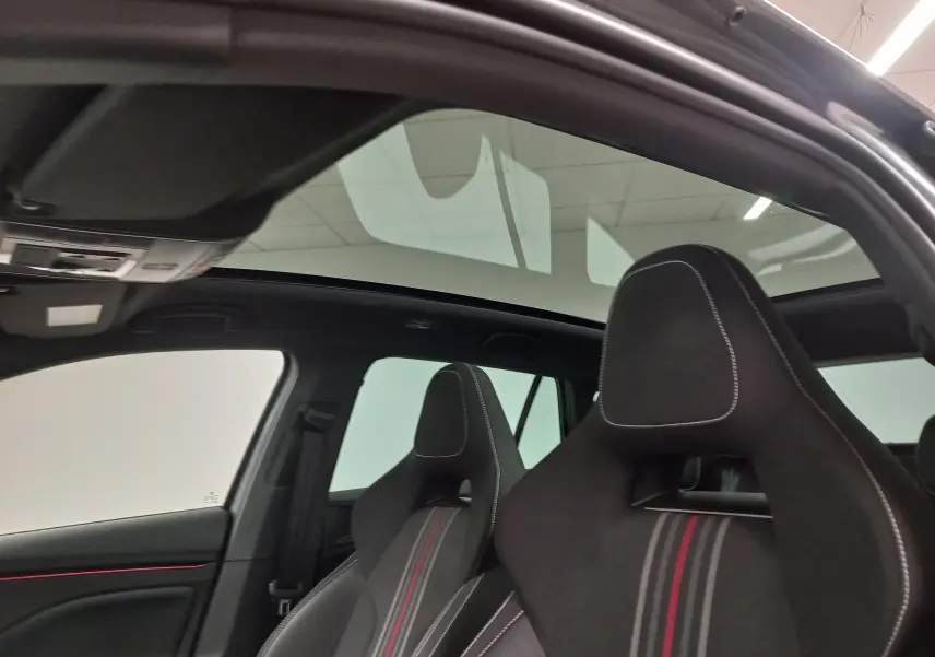 Intérieur de la SKODA SCALA 2025 avec toit panoramique et sièges sport noirs à surpiqûres blanches et bandes rouges.