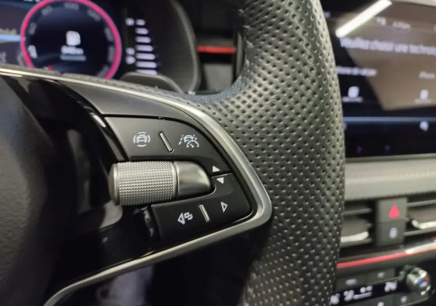 Gros plan sur les commandes du volant perforé noir du Skoda Scala 2025 Monte-Carlo avec tableau de bord numérique en arrière-plan.