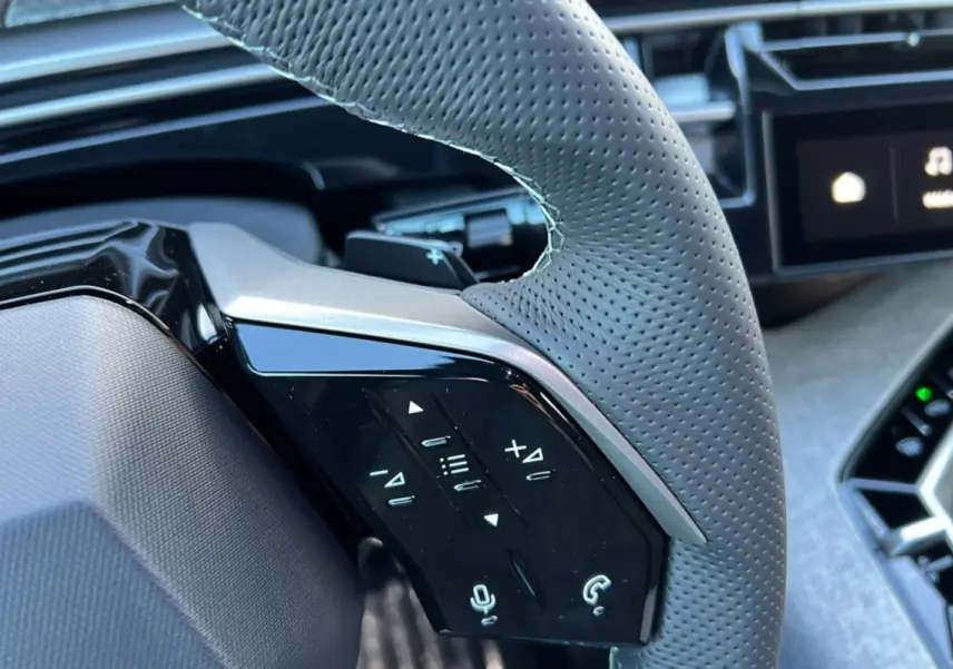 Gros plan sur le volant cuir perforé gris du Peugeot 3008 Hybrid 145 GT avec commandes multifonctions et tableau de bord partiel.