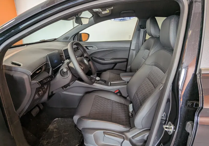 Vue intérieure côté conducteur de la MG3 1,5 HYBRID+ 2026 en Pebble Black, sièges noirs avec surpiqûres orange.