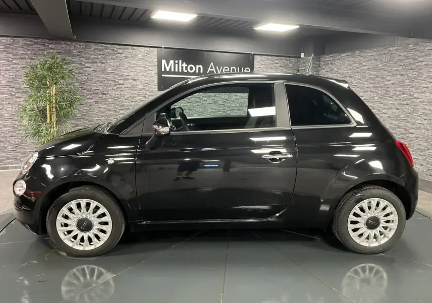 Profil côté gauche d'une Fiat 500 noire 2023 avec jantes alliage et poignées chromées dans un showroom.