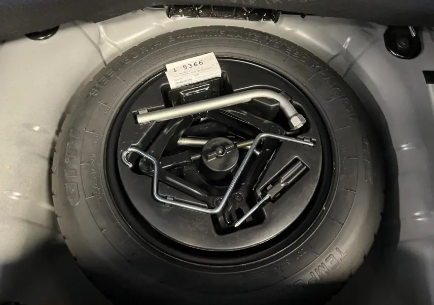 Gros plan sur la roue de secours noire et ses outils dans le coffre de la Fiat 500 Dolcevita noire 2023.
