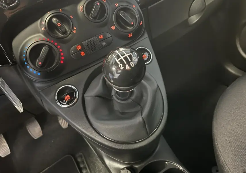 Gros plan sur le levier de vitesses manuel noir et les commandes de climatisation d'une Fiat 500 noire 2023.