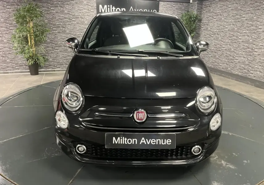 Vue frontale d'une Fiat 500 noire avec calandre chromée et projecteurs ronds dans un showroom.