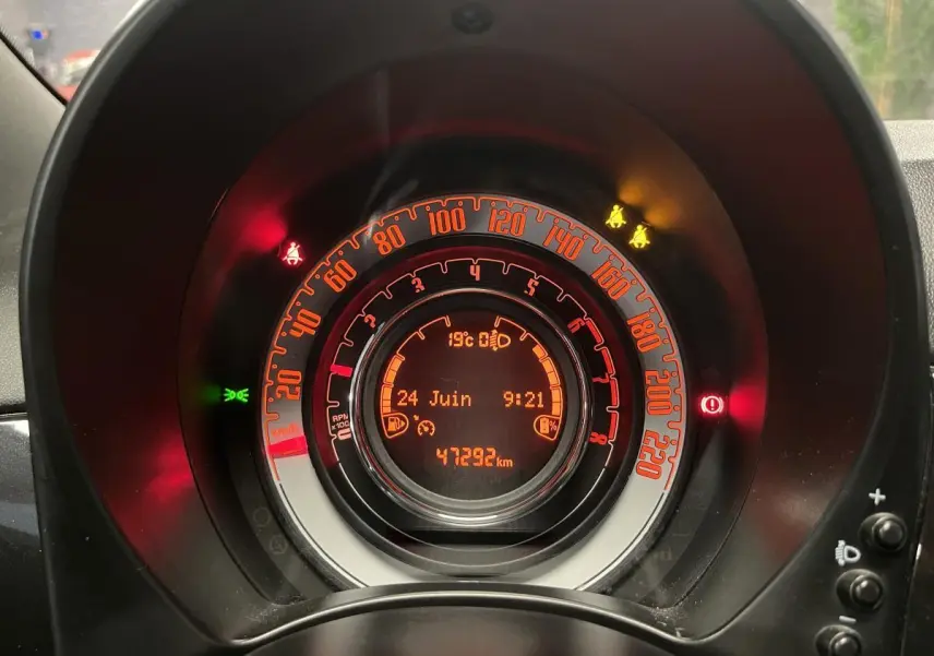 Vue rapprochée du tableau de bord numérique orange de la Fiat 500 noire avec affichage du compteur et témoins allumés.