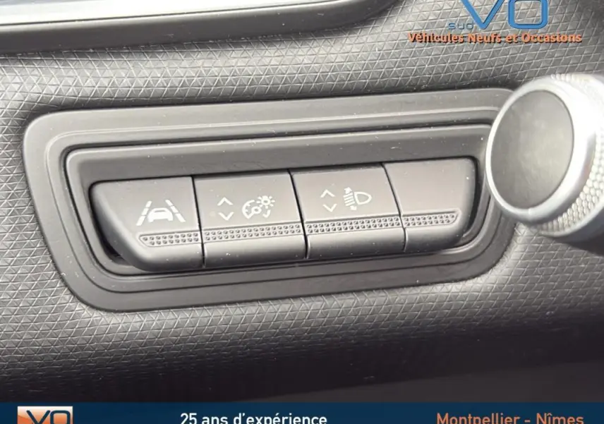 Gros plan sur les boutons de réglage d'aide à la conduite et des feux du tableau de bord d'une Renault Clio gris foncé.