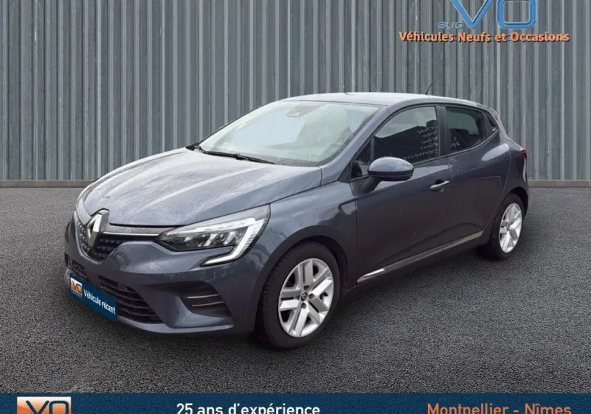 Renault Clio V Blue dCi 85 Business gris foncé vue 3/4 avant droit sur sol bitumé devant un mur métallique.