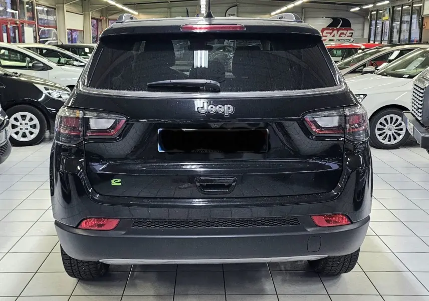 Vue arrière du Jeep Compass noir 2023 avec logo vert hybride, feux arrière et lunette teintée en intérieur showroom.