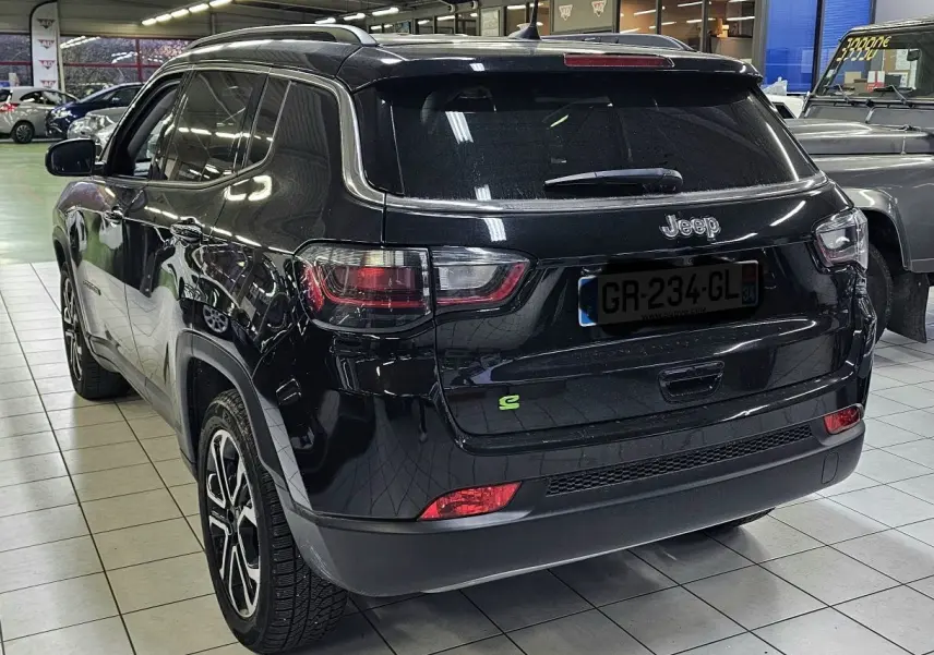 Vue 3/4 arrière d'un Jeep Compass noir brillant en hybride essence, avec jantes alliage et feux arrière LED visibles.