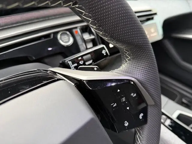 Gros plan sur le volant cuir perforé avec palettes de changement de vitesse et commandes multifonctions du Peugeot 3008 Hybrid GT 2025.