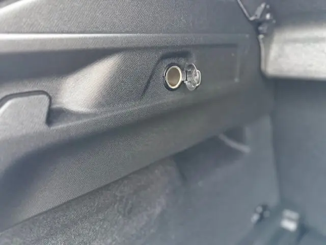 Prise 12 volts ouverte dans le coffre du Peugeot 3008 Hybrid 145 E-DCS6 GT gris titane, vue rapprochée côté droit.