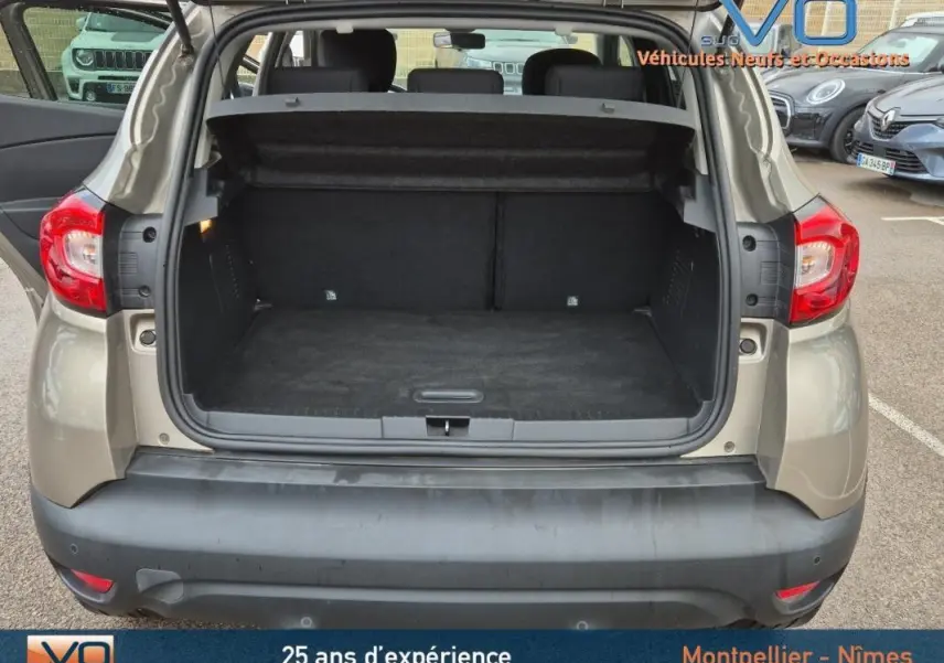 Coffre ouvert vu de l'arrière d'un Renault Captur gris 2014, montrant l'espace de chargement et la plage arrière relevée.
