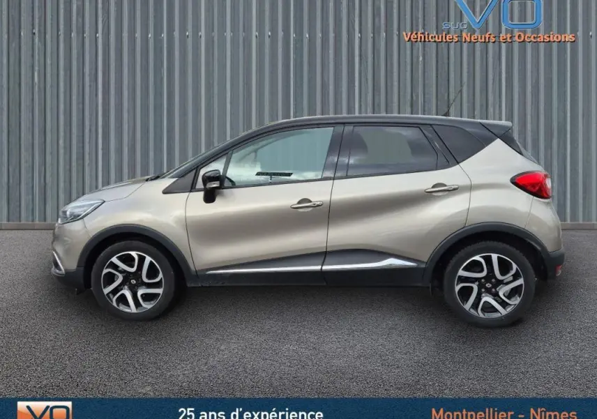 Profil côté gauche d'un Renault Captur gris 2014 avec toit noir et jantes alliage 17 pouces sur fond industriel.