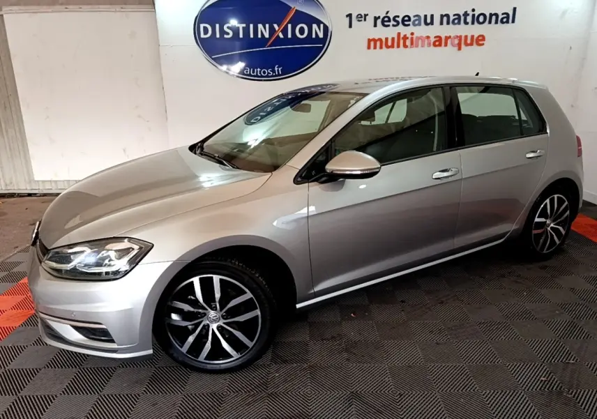 Volkswagen Golf gris clair vue de profil côté gauche, avec jantes alliage et phares allumés.