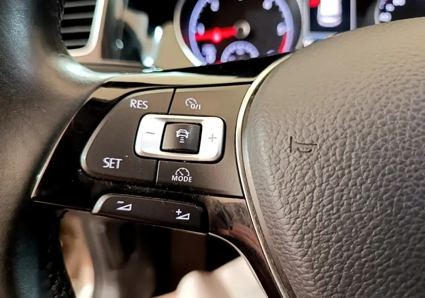 Gros plan sur les commandes du volant cuir gris de la Volkswagen Golf 1.6 TDI 2017 avec tableau de bord lumineux en arrière-plan.