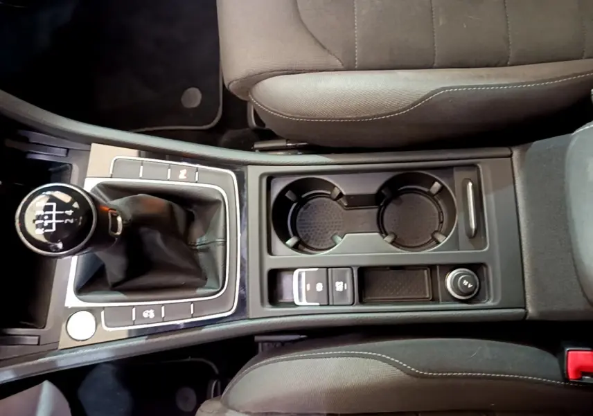 Vue plongeante sur la console centrale de la Volkswagen Golf gris clair, montrant levier de vitesse manuel et porte-gobelets.