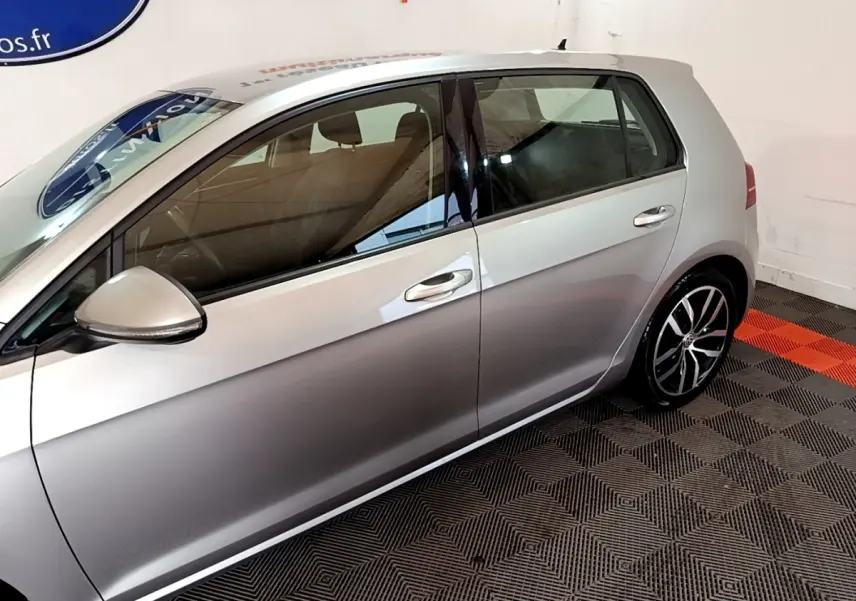 Profil côté gauche d'une Volkswagen Golf gris clair 2017, avec jantes alliage et rétroviseur électrique intégré.