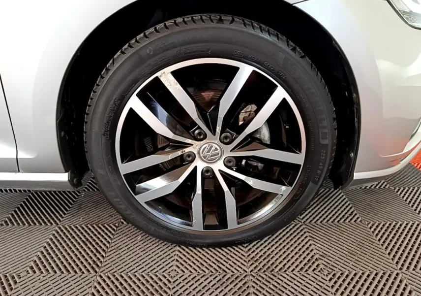 Gros plan sur la roue avant droite d'une Volkswagen Golf gris clair avec jante alliage bicolore.