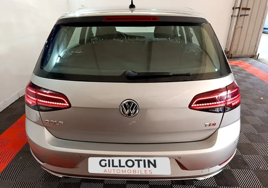 Vue arrière d'une Volkswagen Golf gris clair avec feux LED allumés dans un garage.