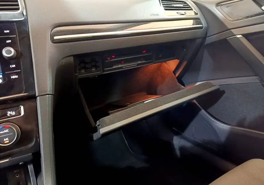 Gros plan sur la boîte à gants ouverte côté passager de la Volkswagen Golf gris clair, avec éclairage intérieur orange.