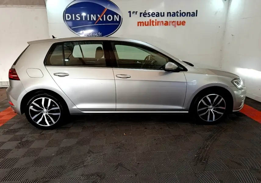 Volkswagen Golf gris clair vue de profil côté gauche, avec jantes alliage et logo Distinxion en arrière-plan.