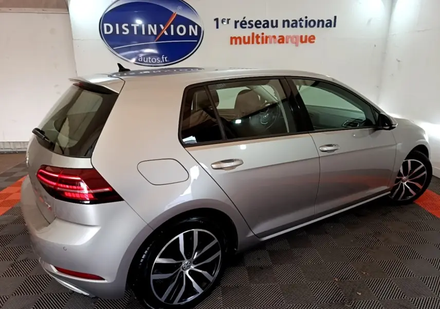 Vue 3/4 arrière droite d'une Volkswagen Golf gris clair 2017 avec jantes alliage et feux arrière LED allumés.
