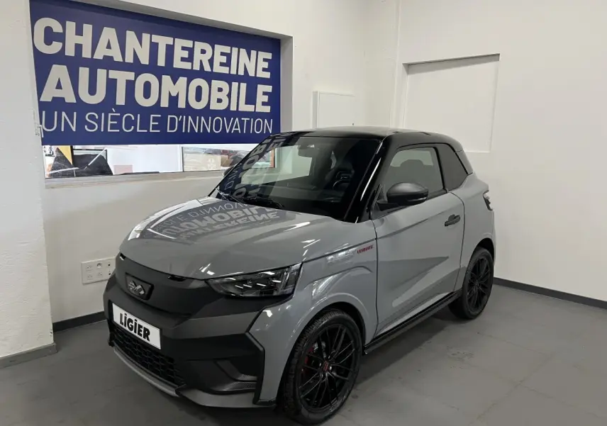 Vue 3/4 avant droite d'une Ligier JS50 0.5 REVO D+ Ultimate gris avec toit noir et jantes noires en showroom.