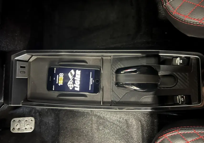 Vue plongeante sur la console centrale noire du Ligier JS50 bleu, avec levier de vitesses et smartphone posé dessus.