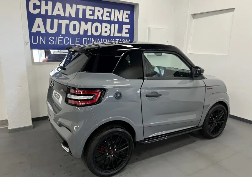 Vue 3/4 arrière droite de la LIGIER JS50 0.5 REVO D+ ULTIMATE grise avec toit noir et jantes noires en intérieur showroom.
