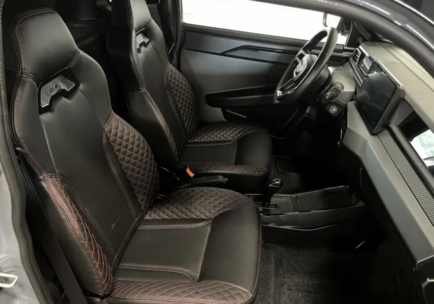 Vue intérieure côté gauche de la LIGIER JS50 0.5 REVO D+ ULTIMATE 2026, sièges noirs avec surpiqûres rouges et tableau de bord moderne.