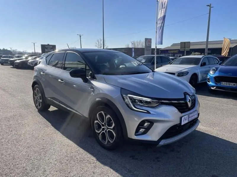 Renault Captur 1.6 E-Tech Hybrid 145 Intense gris métal vu en 3/4 avant droit sur parking ensoleillé.