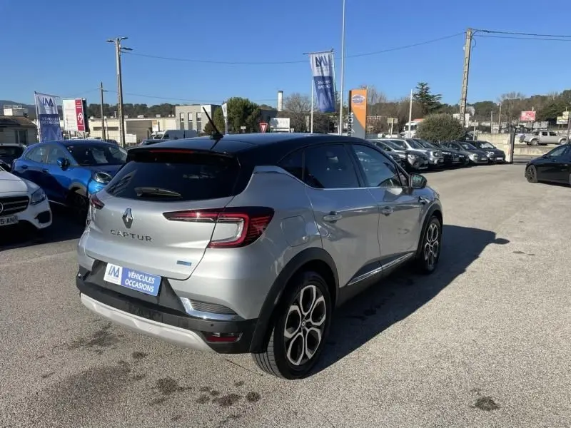 Renault Captur 1.6 E Tech Hybrid 145 Intense gris métal, vue 3/4 arrière droit sur parking ensoleillé.