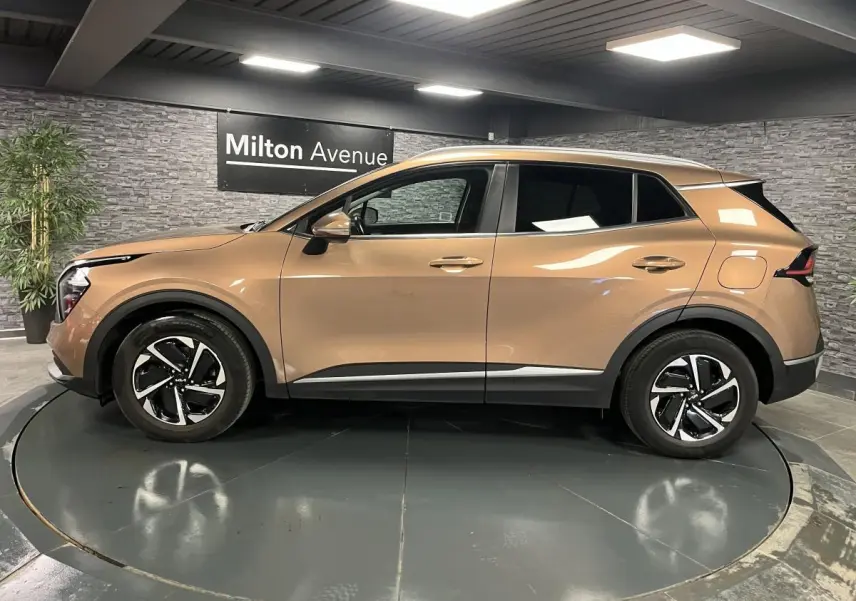 Profil latéral gauche d'un Kia Sportage marron métallisé 2022 avec jantes alliage 17 pouces et protections noires.