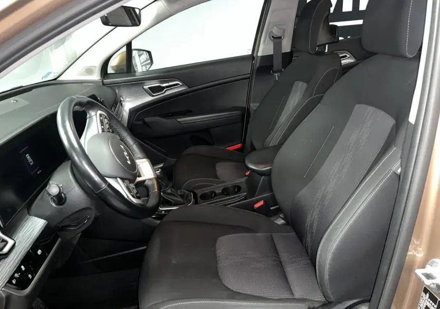 Vue intérieure côté conducteur du Kia Sportage marron 2022, sièges tissu noir et volant cuir avec commandes intégrées.