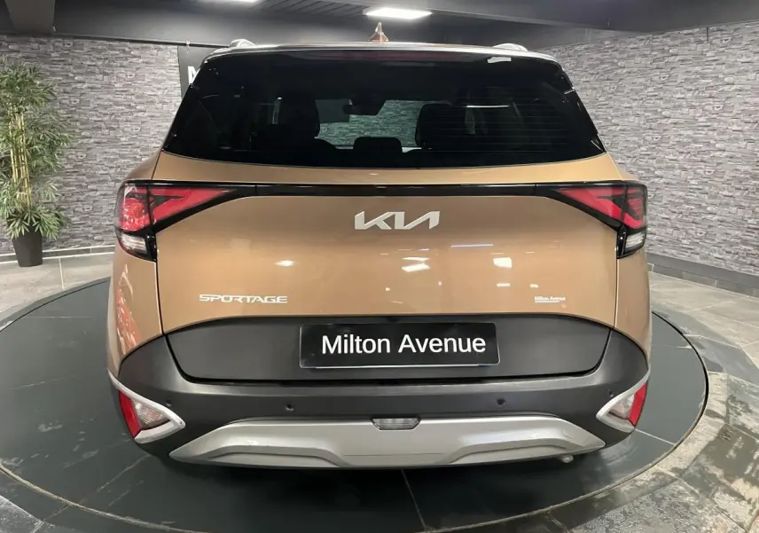Vue arrière d'un KIA Sportage marron métallisé avec bouclier noir et plaque Milton Avenue visible en intérieur showroom.
