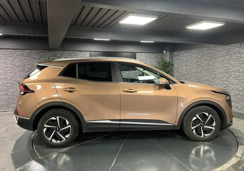 Profil droit d'un KIA SPORTAGE marron métallisé 2022 avec jantes alliage 17 pouces et protections noires laquées.