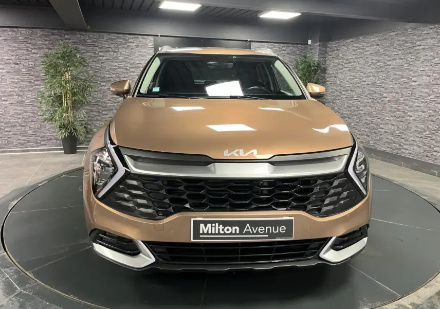 Vue frontale d'un Kia Sportage marron métallisé avec calandre noire et logo KIA sur le capot dans un showroom.